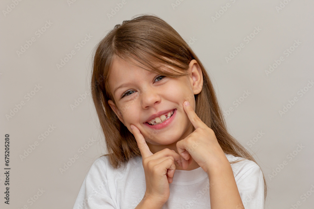Portrait of caucasian happy little girl with open wide smile holding fingers on cheeks showing good teeth looking at camera Portrait of caucasian happy little girl with open wide smile holding fingers on cheeks showing good teeth looking at camera