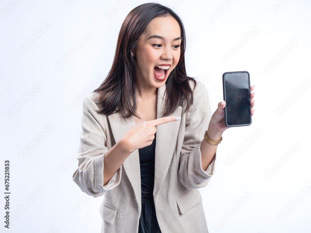 A portrait of an Indonesian Asian woman wearing a cream-colored blazer, showcasing a blank smartphone screen. Isolated against a white background. A portrait of an Indonesian Asian woman wearing a cream-colored blazer, showcasing a blank smartphone screen. Isolated against a white background.