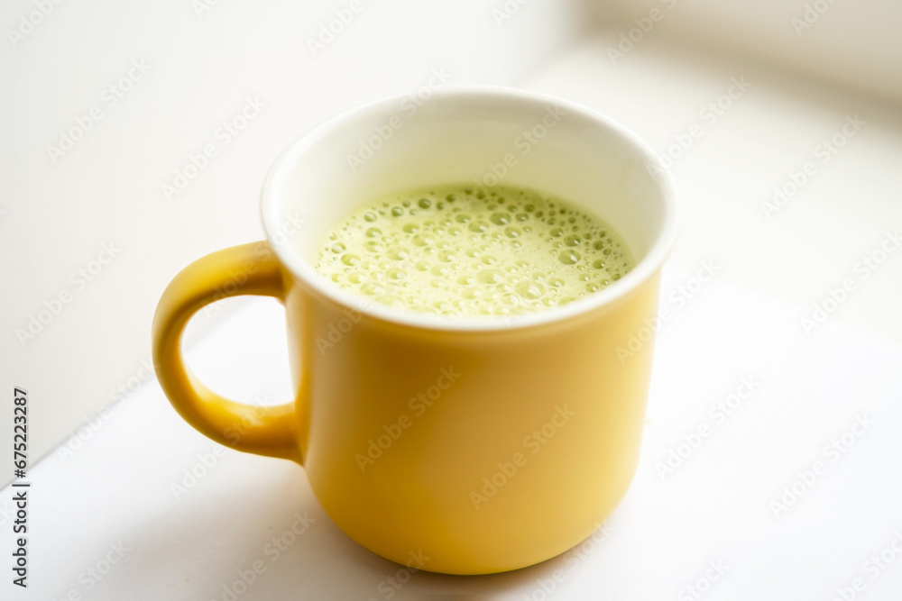 Woman hand is brewing and mixing matcha green latte tea in yellow mug. Isolated on white. Beating with a whisk Woman hand is brewing and mixing matcha green latte tea in yellow mug. Isolated on white. Beating with a whisk