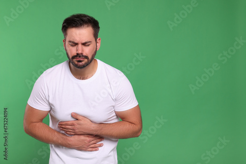Unhappy man suffering from stomach pain on green background, space for text