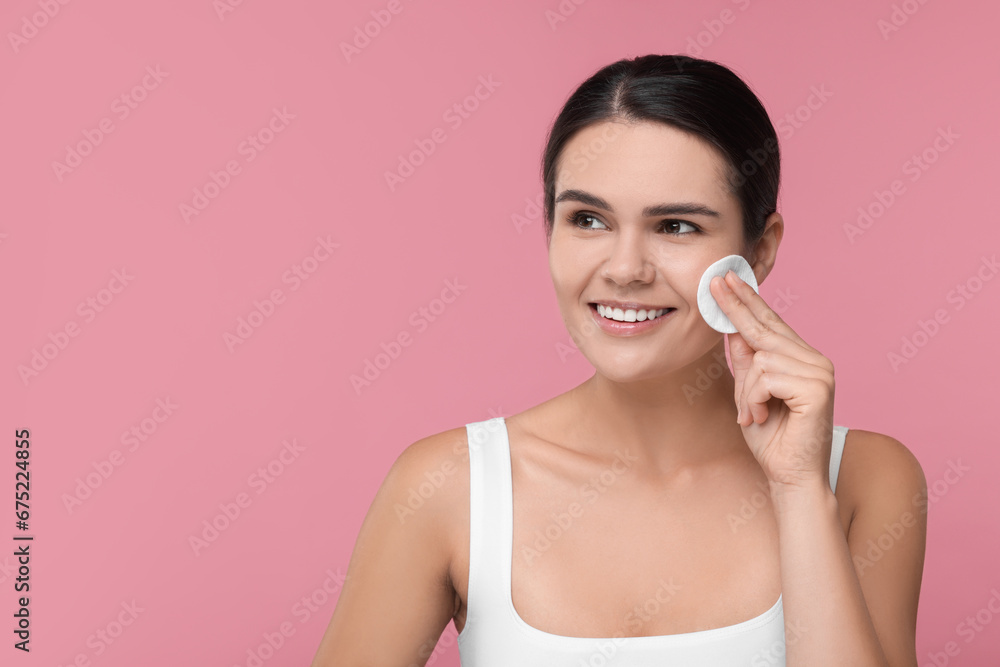 Young woman cleaning her face with cotton pad on pink background. Space for text Young woman cleaning her face with cotton pad on pink background. Space for text