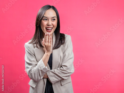 A portrait of an Indonesian Asian woman wearing a cream-colored blazer, posing in surprise and covering her mouth. Isolated against a magenta background.