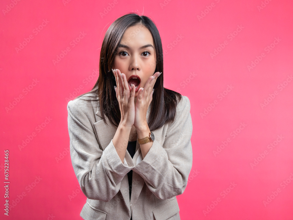 A portrait of an Indonesian Asian woman wearing a cream-colored blazer, looks surprised while opening her hands under her chin. Isolated against a magenta background. A portrait of an Indonesian Asian woman wearing a cream-colored blazer, looks surprised while opening her hands under her chin. Isolated against a magenta background.