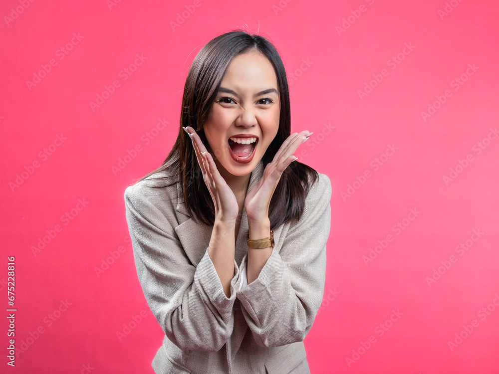 A portrait of an Indonesian Asian woman wearing a cream-colored blazer, looks surprised while opening her hands under her chin. Isolated against a magenta background. A portrait of an Indonesian Asian woman wearing a cream-colored blazer, looks surprised while opening her hands under her chin. Isolated against a magenta background.