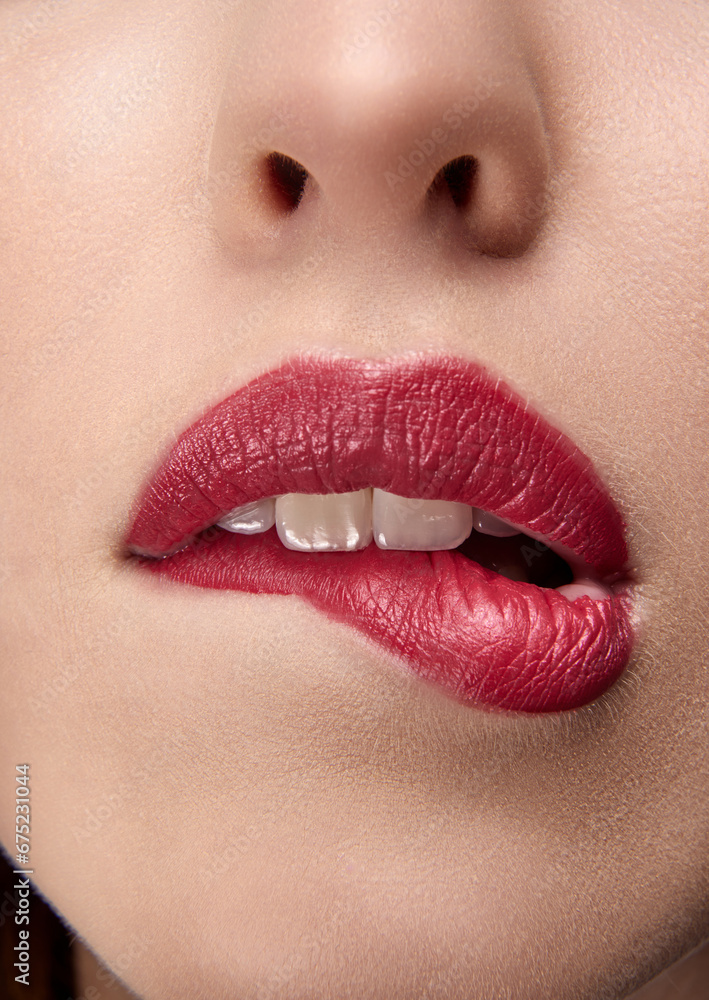 Obraz premium Close up photo of beautiful woman bites her red full plump lips. Portrait of sexy, sensual, seductive lips