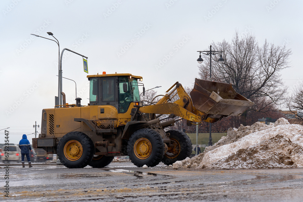 The municipal cleaning service removes snow from city streets. Removing dirty melted snow and ice from city roads using road equipment.