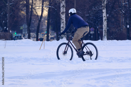 A cyclist rides a bicycle through a snowy park. The man got the season wrong. Outdoor sports in winter, harden.