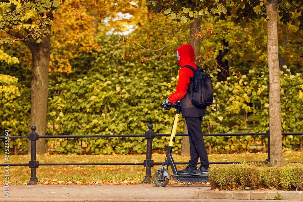 A guy rides along a park path on an electric scooter. Autumn has arrived, the trees in the park are decorated in bright colors. Golden fall. A guy rides along a park path on an electric scooter. Autumn has arrived, the trees in the park are decorated in bright colors. Golden fall.