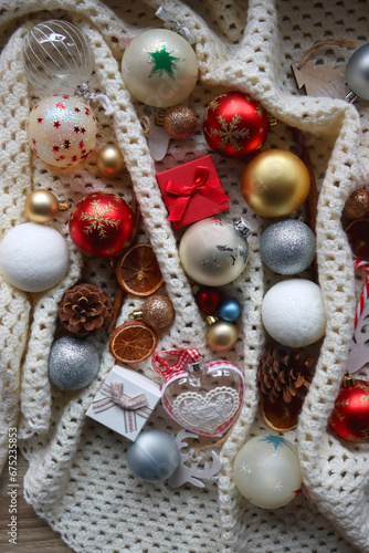 Various colorful Christmas ornaments, small presents and seasonal spices on white knitted blanket. Top view.