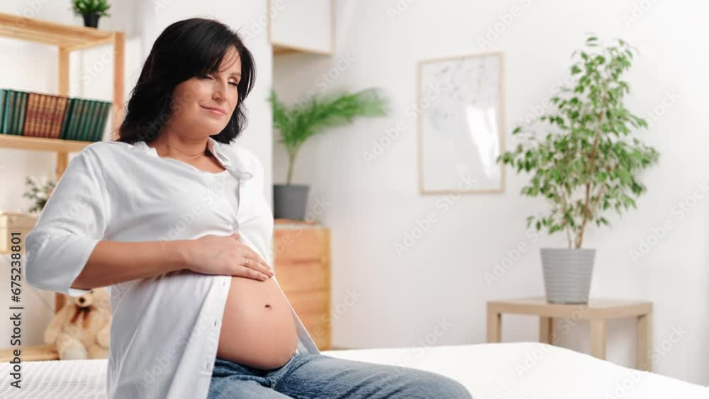 Happy brunette pregnant woman stroking belly enjoy peaceful tranquility relaxing on bed at home Happy brunette pregnant woman stroking belly enjoy peaceful tranquility relaxing on bed at home