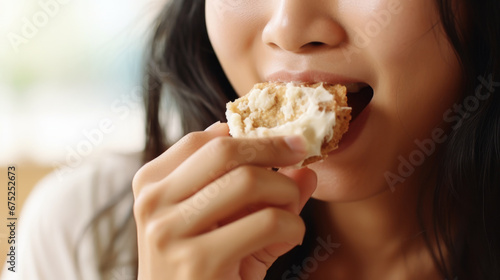Young beautiful asian woman eating a cake with cream closeup