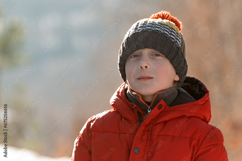 Portrait of child boy in red jacket and knitted hat in winter outside in bright sunny day. Happy red-cheeked guy outside Portrait of child boy in red jacket and knitted hat in winter outside in bright sunny day. Happy red-cheeked guy outside