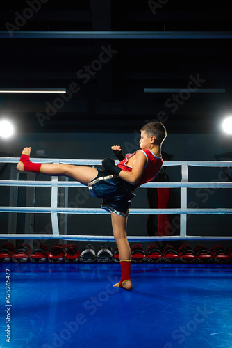 full length portrait of little athletic boy, professional martial arts sportsman in uniform performing kicks on ring.