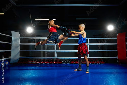 Two serious boys, kids, kickboxers, professional martial arts sportsmen performing kicks, training on ring at gym.