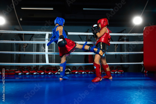 Healthy boy, kickboxer in uniform training kickboxing with sparring partner in ring at sport gym. Pupil sportsmen. © Lustre
