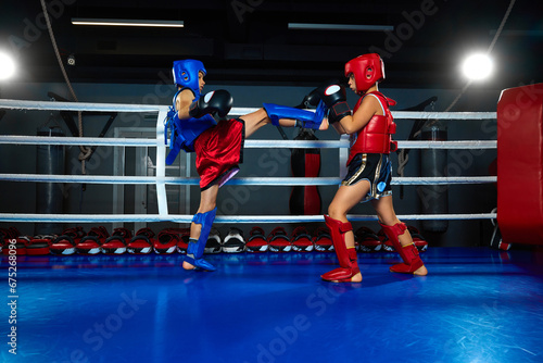 Competitive boy, kickboxer in uniform training kickboxing with sparring partner in ring at sport gym. Pupil sportsmen.