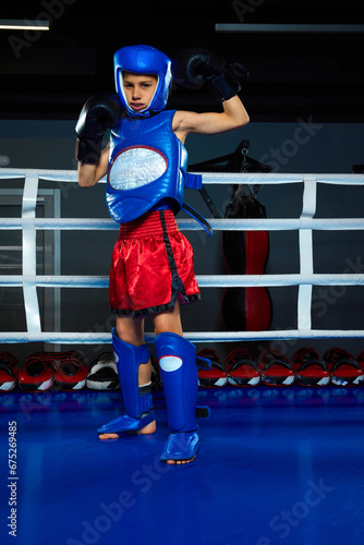 One little sportsman, boy in mouth guard dressed in uniform and protective gloves standing, posing on ring.