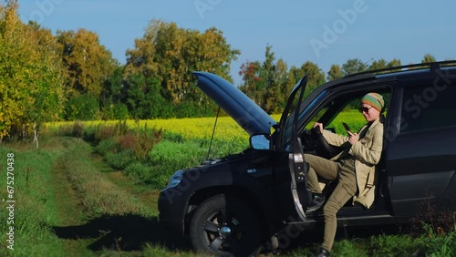 A frustrated female driver sitting in the car calling roadside service insurance. Road trip accident. Car breakdown drove into a ditch in a deserted countryside. photo