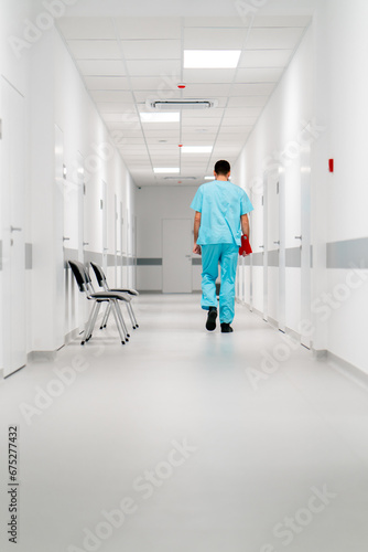A tall male doctor with a beard walks along the hospital corridor with folder of documents © Guys Who Shoot