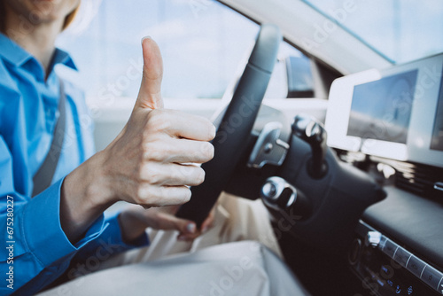 Woman sitting in electric car and showing thumbs up sign photo