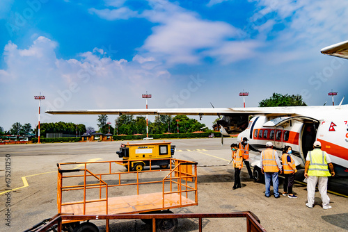 Kathmandu, Nepal - May 15, 2023 : A view of a small aircraft and staff people including airport vehicles.Short flight taking passengers to lukla airport. Blue sky with clouds and greenery in backdrop.