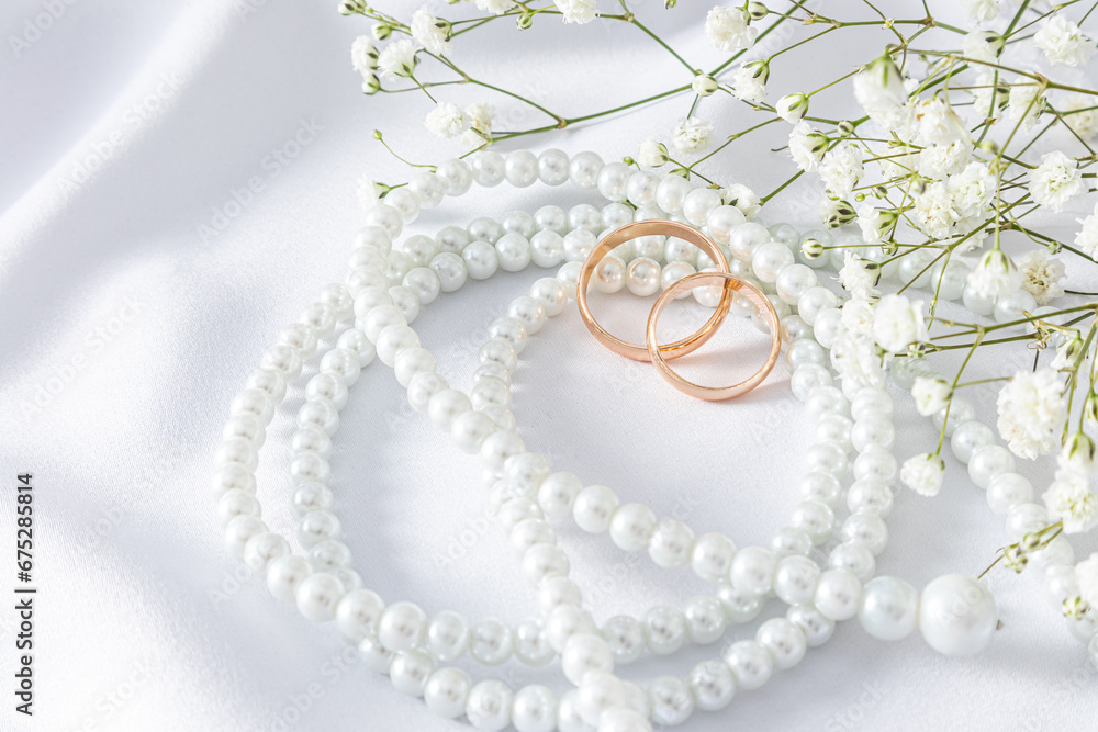 Two gold wedding rings on a white satin background with chic pearl beads and a gypsophila branch. Top view. postcard. Layout for design. invitation. Two gold wedding rings on a white satin background with chic pearl beads and a gypsophila branch. Top view. postcard. Layout for design. invitation.