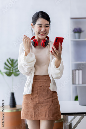 Happy young Asian woman using Phone sitting at desk  studying online  looking at phone screen learning web classes or having virtual call meeting remote working from home.