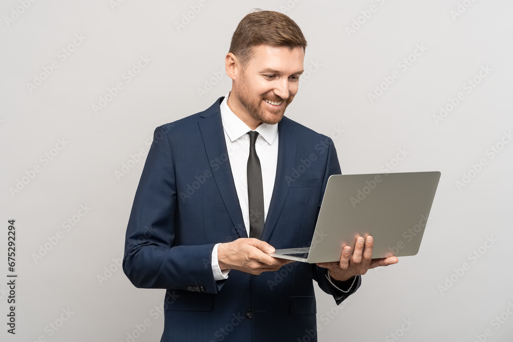 Successful man smiling broadly, looking at laptop screen. Satisfied facial expression, good offer, transaction, business video call. Studio portrait businessman with computer, isolated on gray wall. Successful man smiling broadly, looking at laptop screen. Satisfied facial expression, good offer, transaction, business video call. Studio portrait businessman with computer, isolated on gray wall.