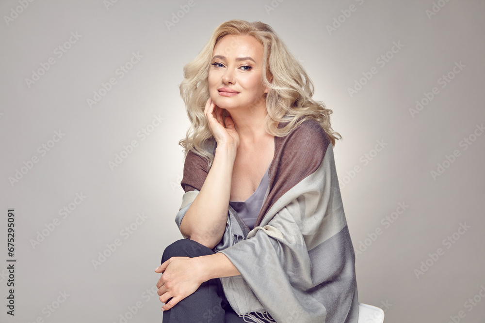 Mature older woman wearing in tippet plaid sitting on chair over grey isolated. Mature older woman wearing in tippet plaid sitting on chair over grey isolated.