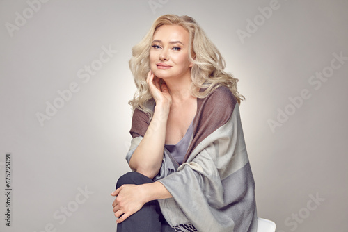 Mature older woman wearing in tippet plaid sitting on chair over grey isolated. photo