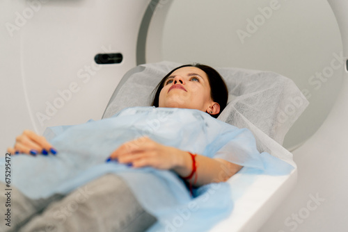 A girl in a medical gown lies on a movable couch of a magnetic resonance imaging machine and prepares for diagnosis photo