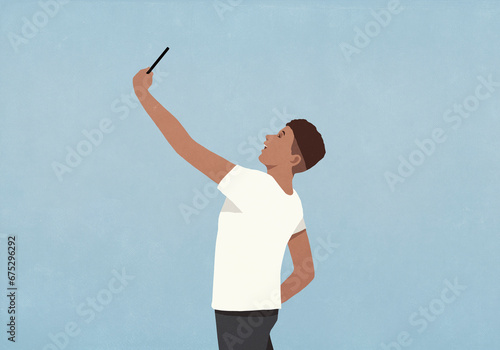 Young man with arm raised taking selfie with smart phone on blue background
 photo