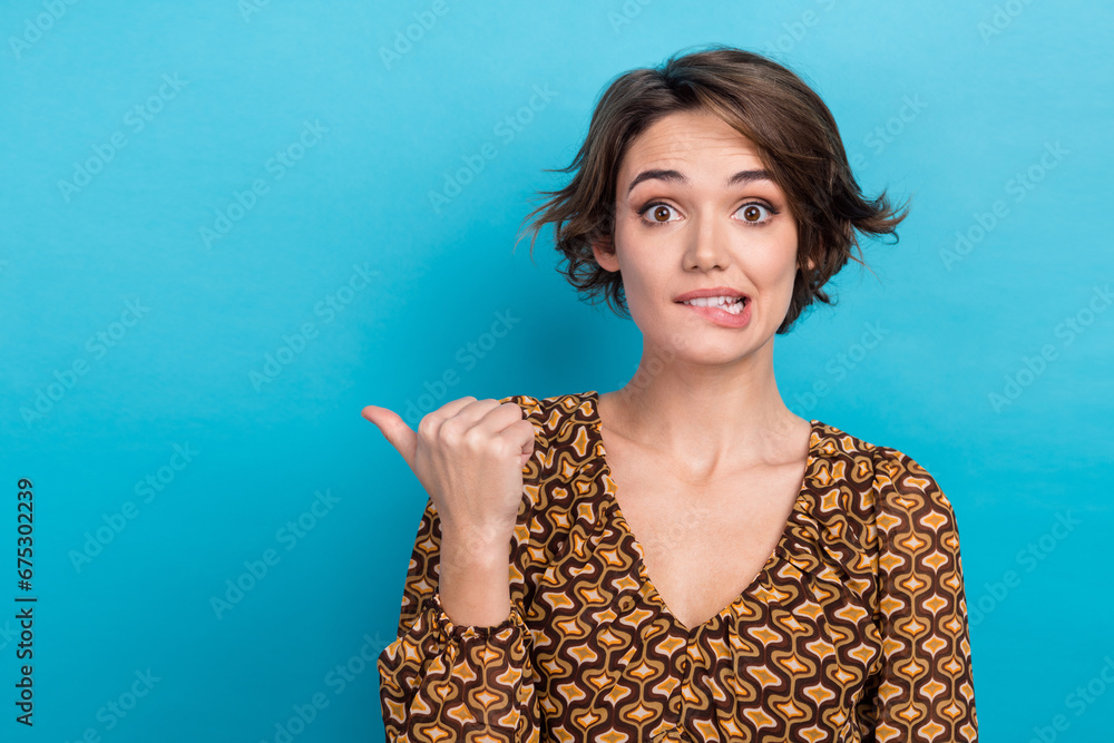 Photo of pretty nervous person biting lips indicate thumb finger empty space isolated on blue color background - obrazy, fototapety, plakaty 