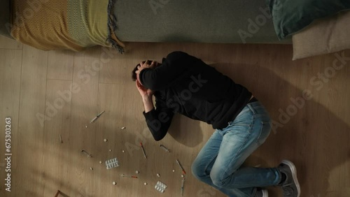 Top view of a man lying on the living room floor among pills, syringes, close up. The man is suffering from withdrawal after taking drugs. Drug addiction are killers of mental and physical health.