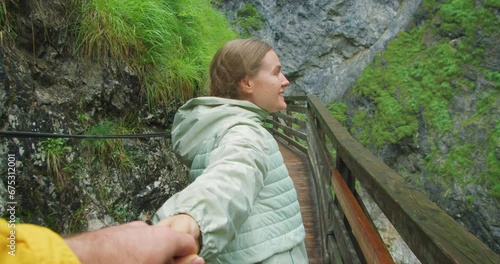 Girl walking along the duckboards in rocky gorge. A woman holds a man's hand and calls him to follow her. Mountain landscape in autumn. photo