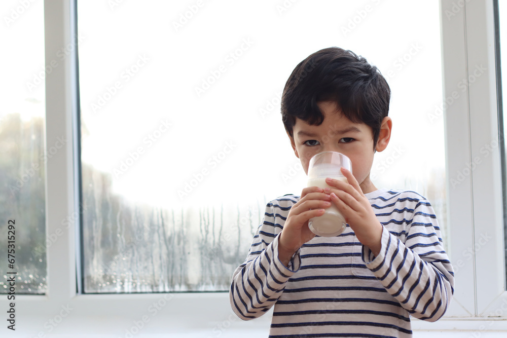 child drinking milk and holding glass of milk sunrise breakfast morning near window. child drinking milk and holding glass of milk sunrise breakfast morning near window.