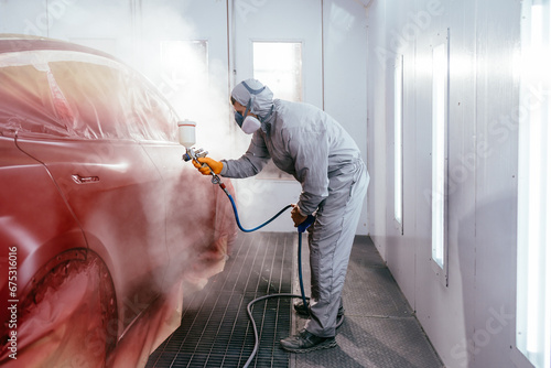 Automotive paint services, quality auto body shop concept. Repairman painter in chamber painting automobile car.