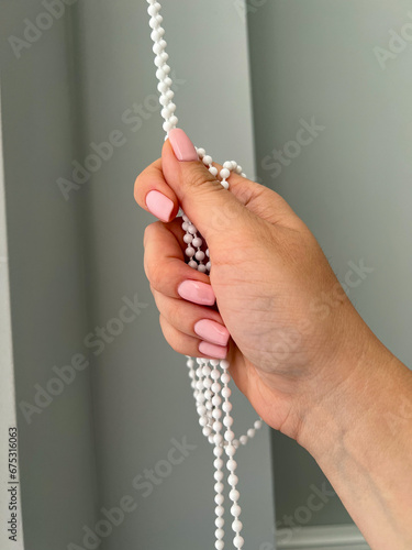 A female hand holding a beaded chain for the blinds