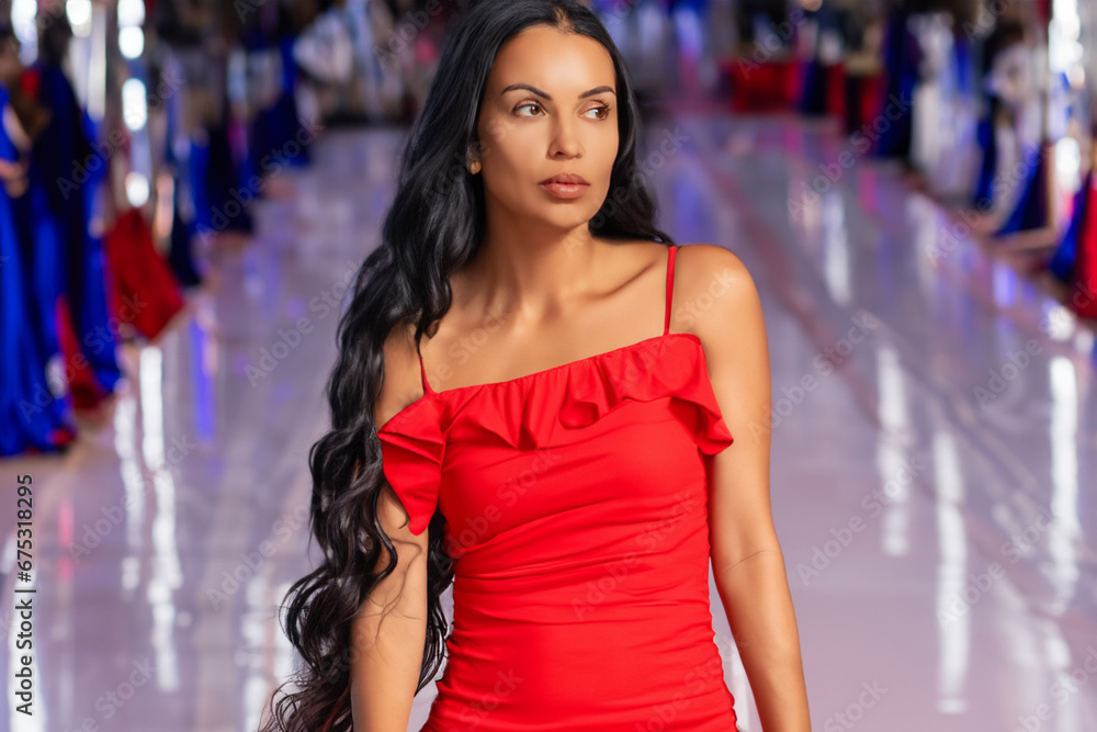 beautiful woman in a dress defiles. a brunette in a bright red dress walks along the catwalk, many people in the background. modeling business concept