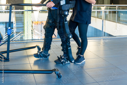 Mechanical exoskeleton. Female physiotherapy doctor helping unrecognizable disabled person with robotic skeleton to walk. Futuristic rehabilitation, Physiotherapy in a modern hospital