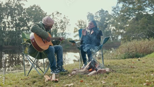 Camping, fire and music with a guitar couple in nature, bonding together in the wilderness for romance or dating. Hiking, travel or instrument with a man musician and woman by a lake in the forest photo