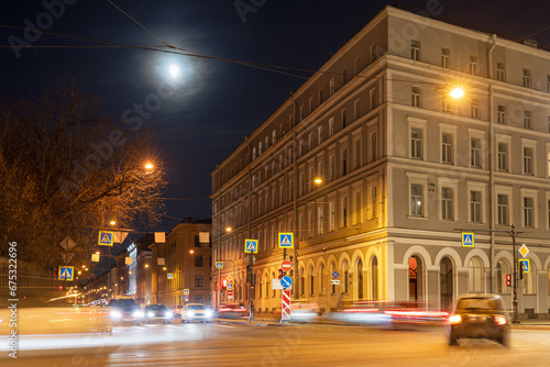 Evening cityscape. Cars drive through the streets of the city at night. Bright moon in the sky. Long exposure. Blurred traces from car headlights. Historical center of St. Petersburg, Russia. © Andrei Stepanov