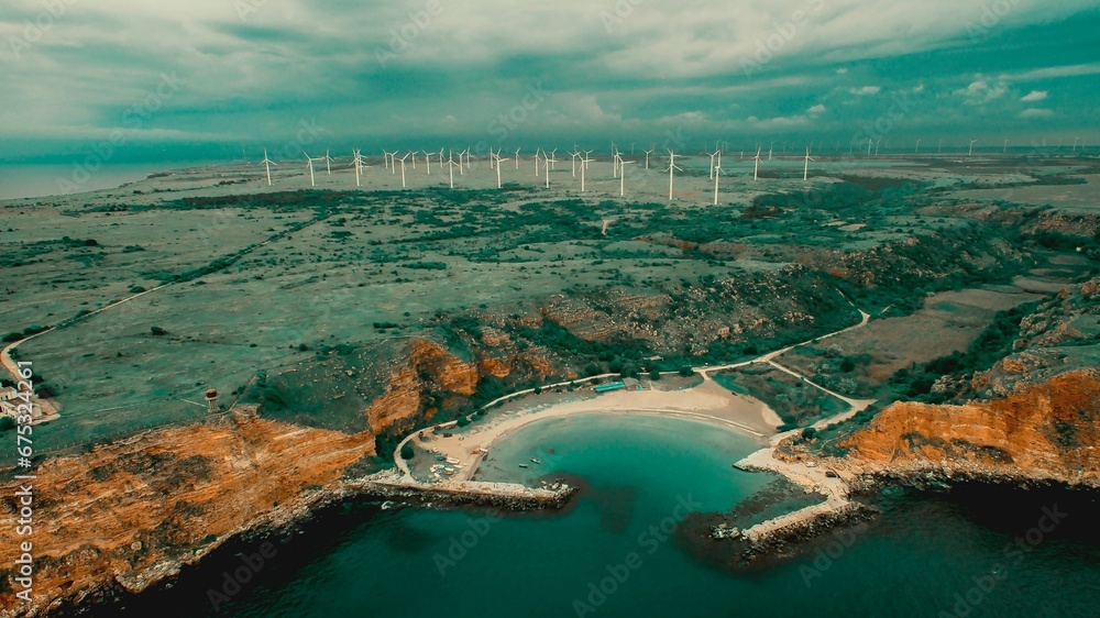 Aerial view of a small island shoreline featuring multiple wind turbines in the background