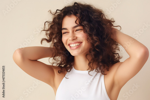 Beautiful young woman with black curly hair in white sleeveless top smiling standing by the window. Sunlight. Banner for beauty skin body care bio eco cosmetics concept photo