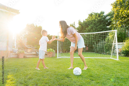 Young mother and son giving five during soccer game in the garden. Happy family playing football, having fun together. Fun Playing Games in Backyard Lawn on Sunny Summer Day. Motherhood, childhood © okrasiuk