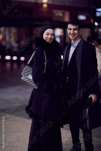 Happy multicultural business couple walking together outdoors in an urban city street at night near a jewelry shopping store window.