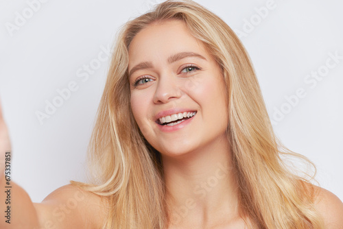 Close up shot of attractive blonde girl with wonderful long hair taking selfie on studio background, beauty concept, copy space