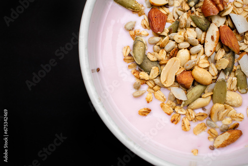 Imagen horizontal de un yogurt de fresa con granola o frutos secos sobre un fondo negro aislado representando un desayuno nutritivo