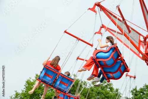 Kids having fun in ferris wheel with chains, carousel ski flyer in amusement park. Happy children, twins having fun outdoors on sunny day. High quality photo
