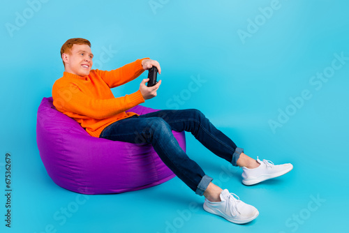 Full length photo of funny gamer man sitting beanbag with playstation isolated teal color background